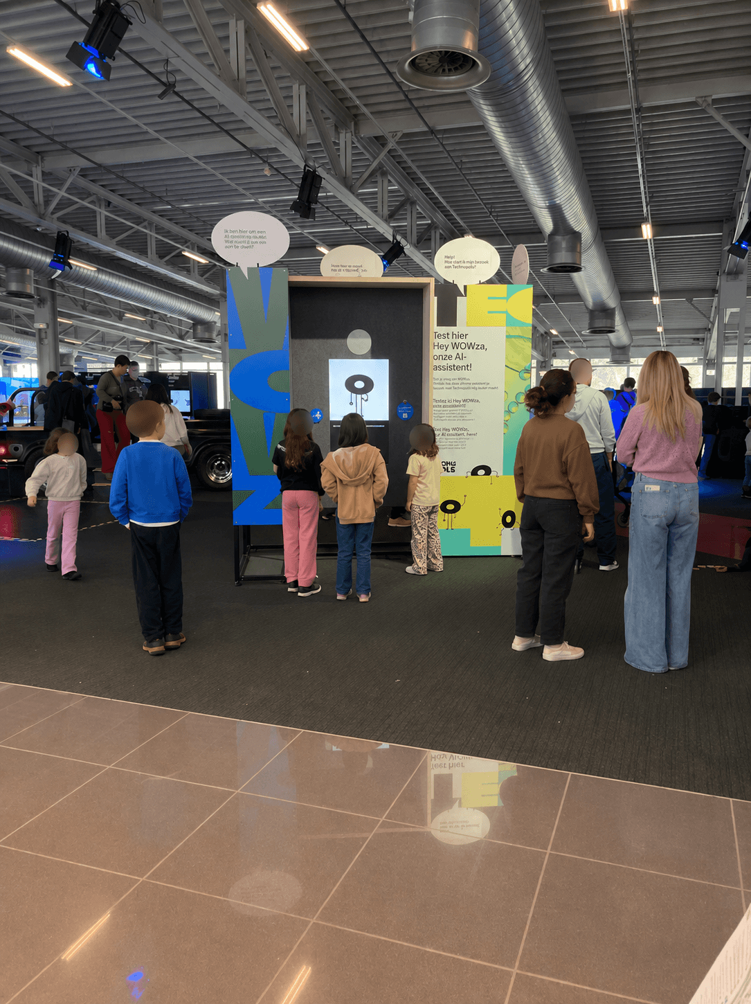 The full heyWowza setup at the Technopolis entrance with children gathered in front of the screen, faces blurred for privacy